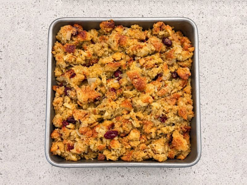 Baked apple and cranberry dressing, dotted with dried cranberries, in a square pan