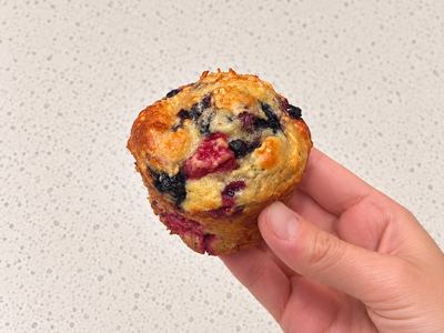 A golden raspberry-blueberry oat muffin held in one hand, with berries on top